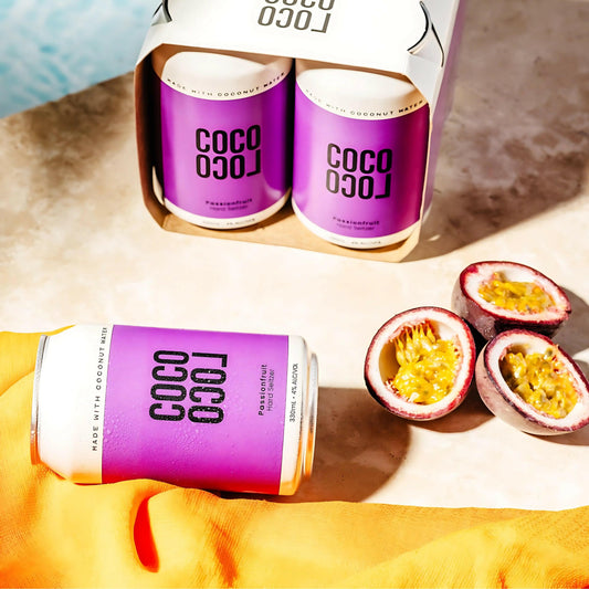 Cans of Coco Loco Passionfruit with passion fruits on a textured surface