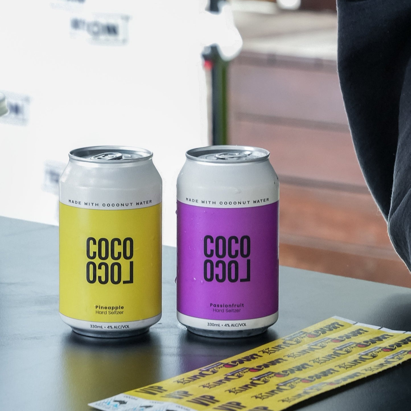 Two cans of COCO LOCO coconut hard seltzer on a bar with festival wrist bands.