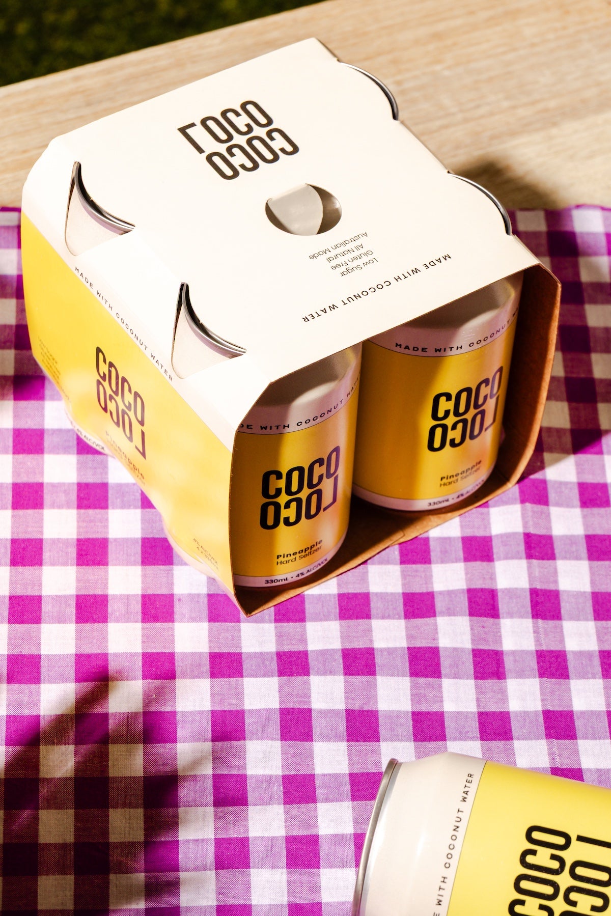 Cans of COCO LOCO Pineapple hard seltzer 4-pack on a pink and white checkered tablecloth