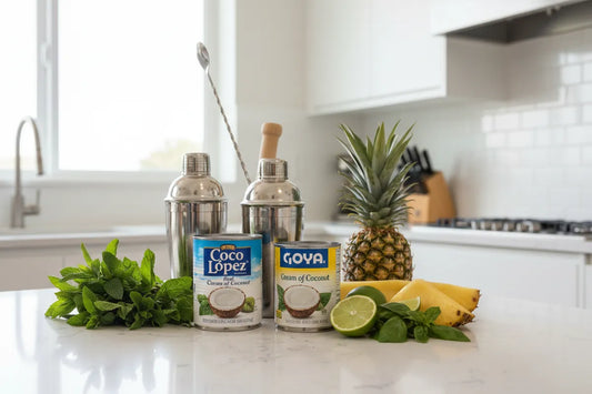 Coco López and Goya cream of coconut cans on a kitchen bench with fresh herbs and fruit