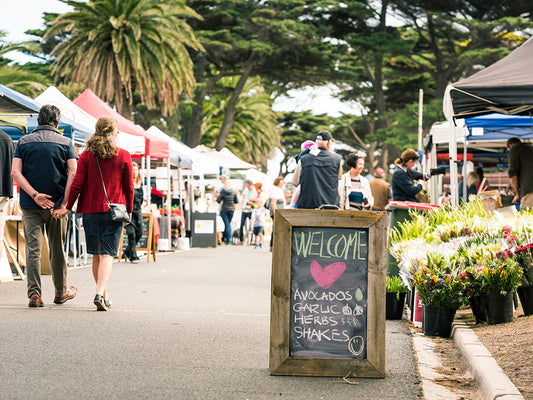 Farmers market with line of marquees and shoppers walking and buying local alcohol