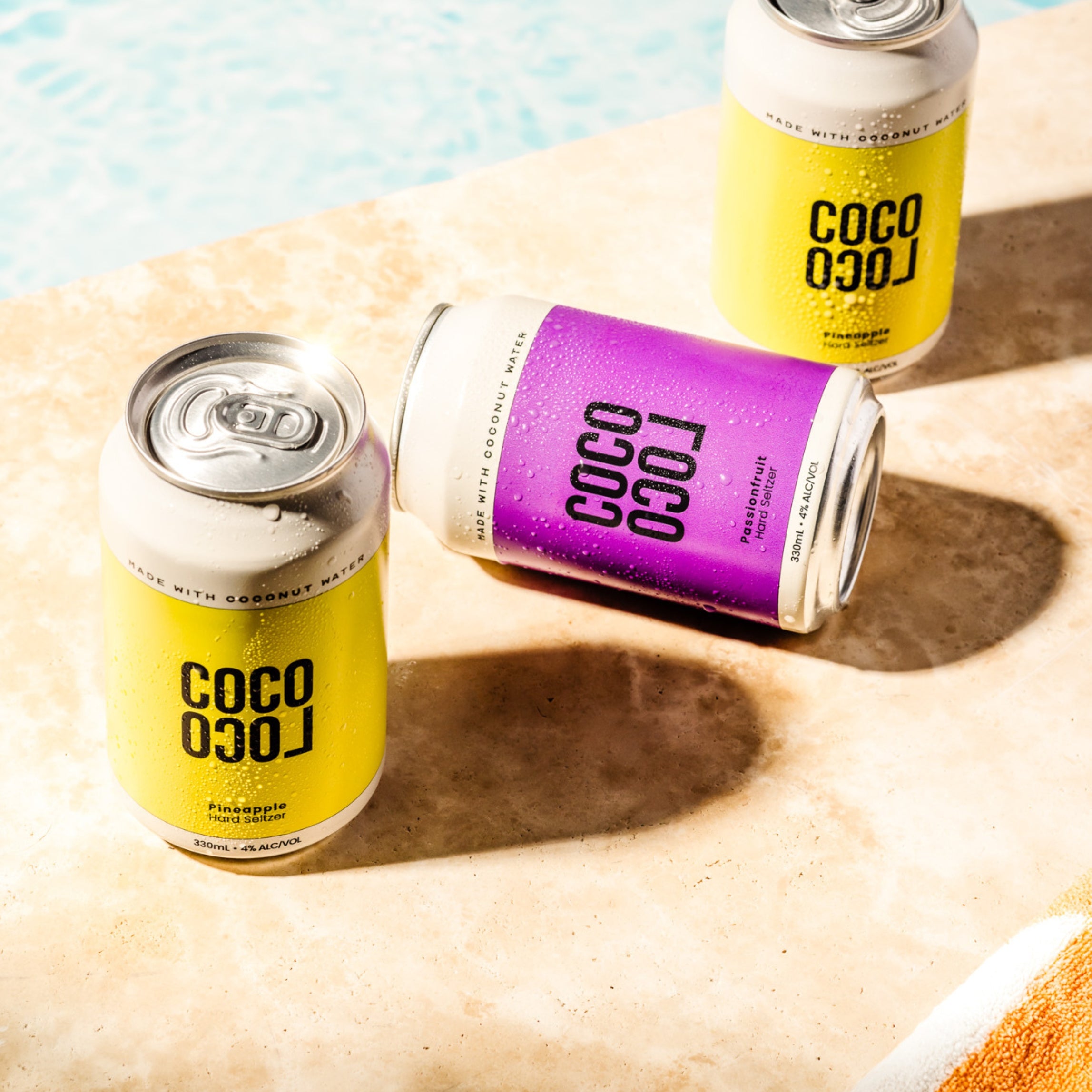 Coco Loco Hard Seltzer collection of cans showing Pineapple and Passionfruit coconut water in sunny poolside setting