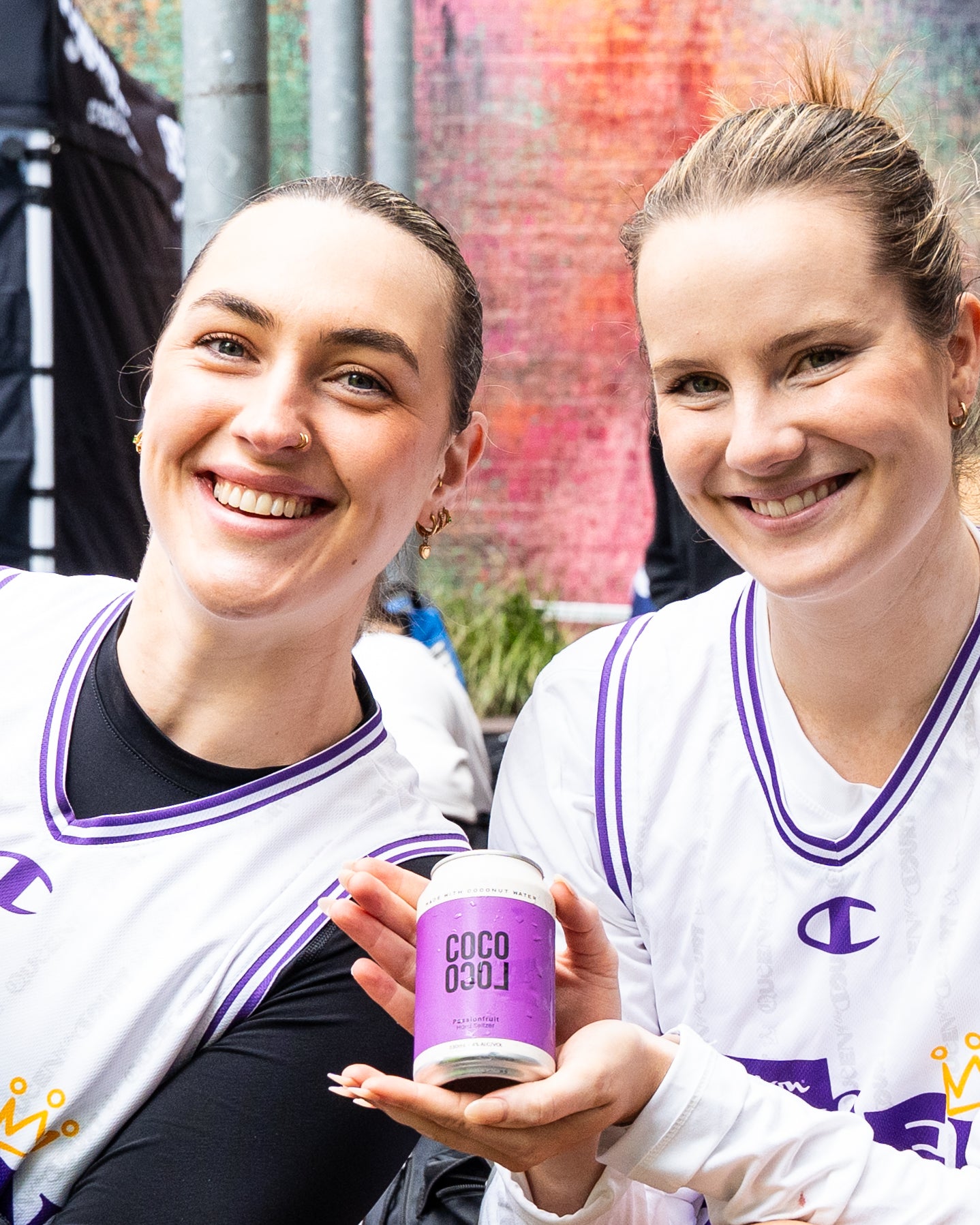 Two women holding a purple can of 'Coco Loco' passiona drink against a colourful background.