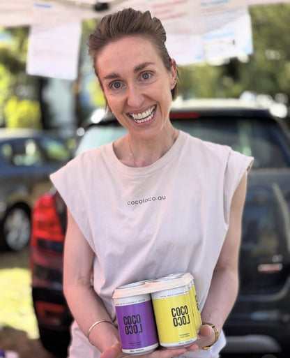 Jill holding Coco Loco Passionfruit and Pineapple cans at a market stall