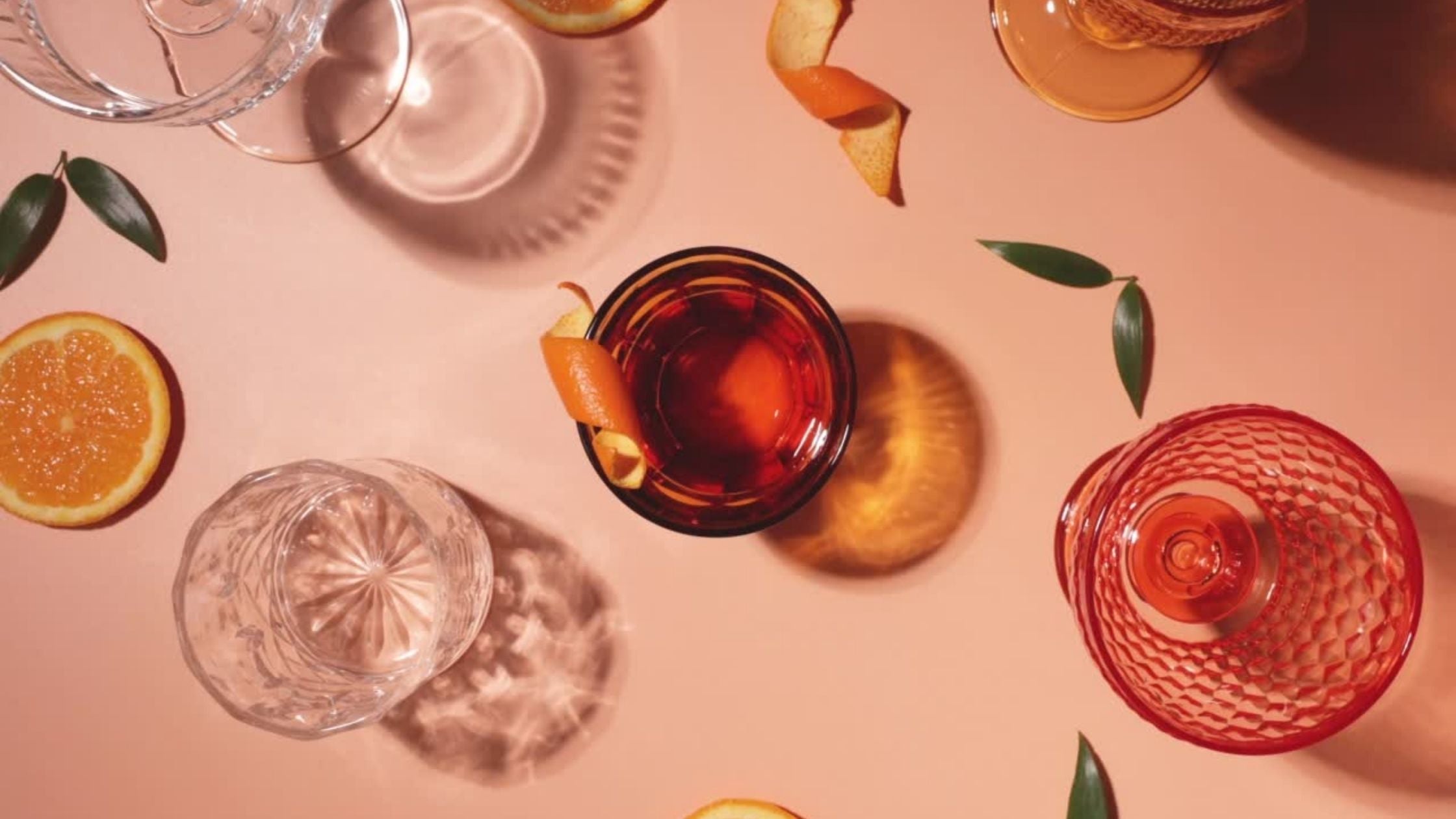 coco loco drinks in glasses and cocktail spritz with orange peel garnish in a glass on a pink background