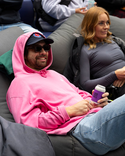 Person wearing a pink hoodie and sunglasses sitting on a couch with a can of Coco Loco passionfruit seltzer.
