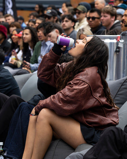 Woman in brown leather jacket drinking a Coco Loco purple drink in a crowded area