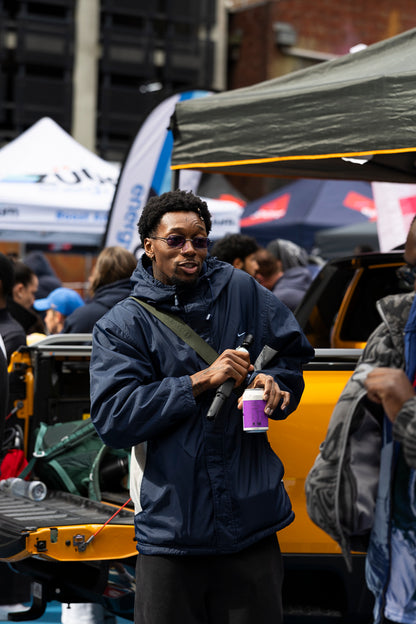 Man in a blue jacket holding a passionfruit hard seltzer on a city street.