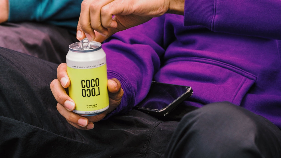 Person in a purple hoodie opening a can of Coco Loco Pineapple hard seltzer