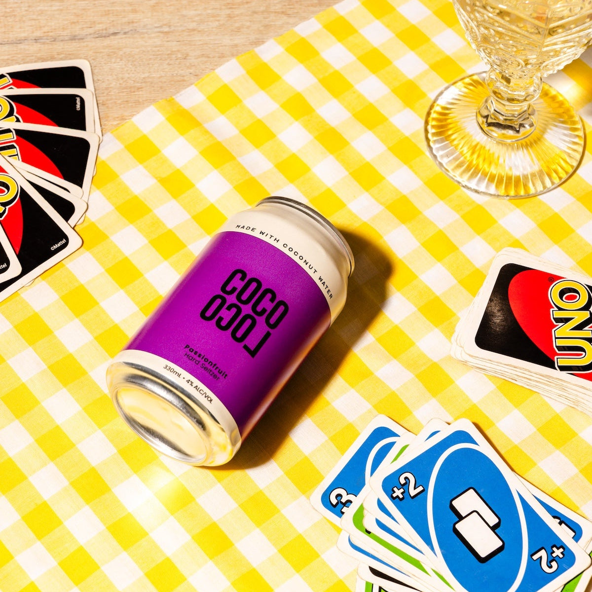 Coco Loco Passiona can on a yellow checkered tablecloth with playing UNO and wine glasses.