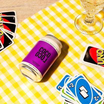 Coco Loco Passiona can on a yellow checkered tablecloth with playing UNO and wine glasses.