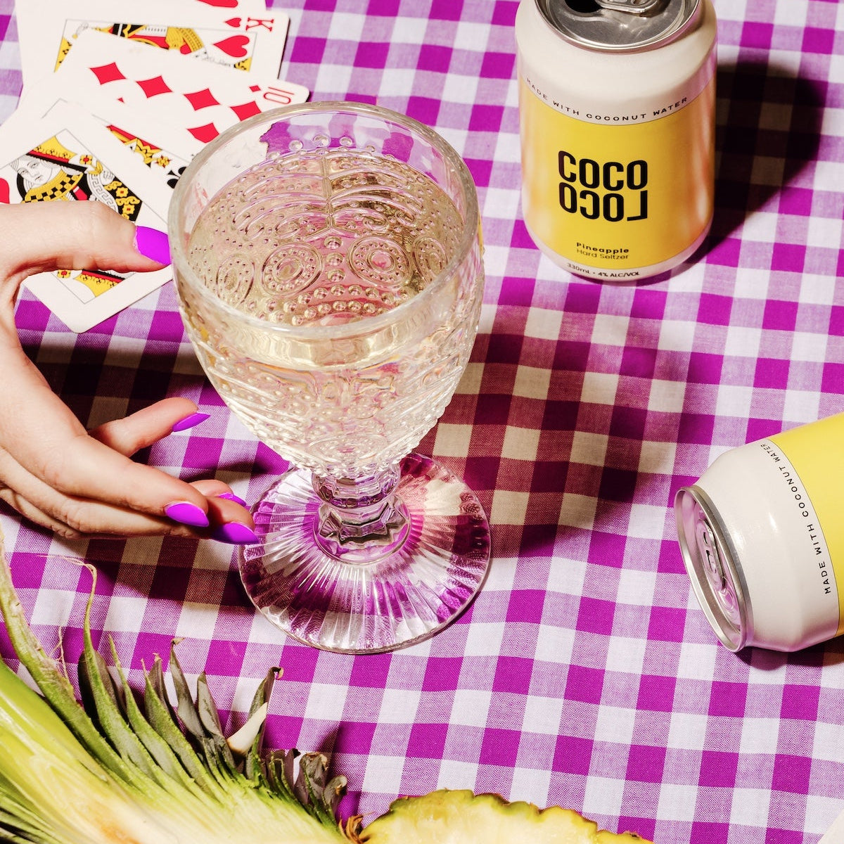 Coco Loco Pineapple Coconut Seltzer can with a glass of a clear drink on a checkered tablecloth.