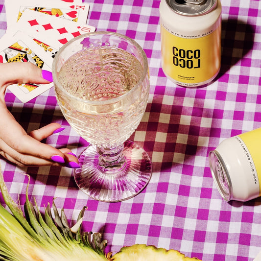 Coco Loco Pineapple Coconut Seltzer can with a glass of a clear drink on a checkered tablecloth.