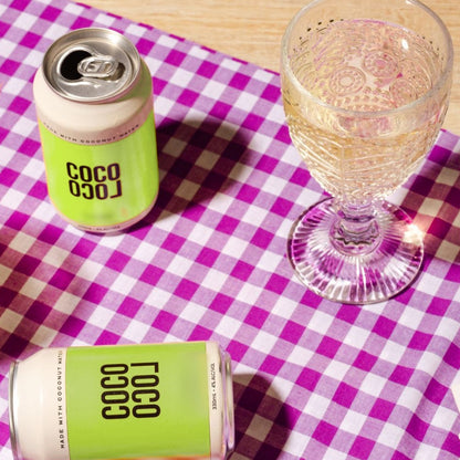 An open Coco Loco Margarita can beside a glass of chilled lime seltzer on a purple gingham tablecloth